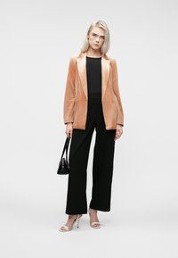Blazer en velours pêche avec revers en satin, design à double boutonnage, associé à un haut noir et un pantalon noir à jambes larges. Accentué par un petit sac noir.