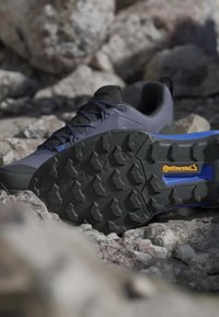Trailové bežecké topánky so šedým zvrškom, čiernou textúrovanou podrážkou a výraznými modrými akcentmi. Na viditeľnom mieste je logo Continental a robustný dezén podrážky.