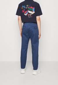 Marineblauwe katoenen broek met een rechte pasvorm, voorzien van achterzakken en een gladde textuur. Gecombineerd met een zwart shirt met korte mouwen en kleurrijke borduursels.