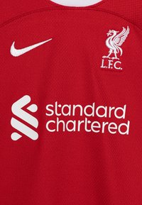 Červený sportovní dres vyrobený z texturované látky s bílým logem Nike, emblémem L.F.C. a nápisem "standard chartered" v tučném bílém písmu.