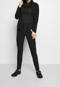 Musta urheilujakku ja tiukka paita, yhdistetty mustiin slim-fit-housuihin ja mustiin jalkineisiin, jossa on sileä kangas ja minimalistinen muotoilu.