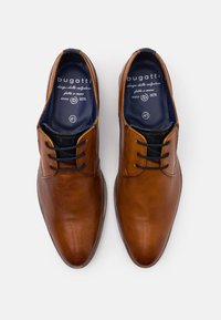 Chaussures en cuir marron avec une finition lisse, bout pointu et design à lacets. L'intérieur est doté d'un revêtement bleu foncé et du logo de la marque. Taille 41.