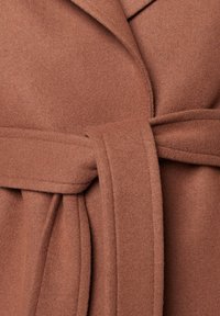 Gros plan d’un manteau en laine marron noué à la taille avec une ceinture en tissu assorti et des détails de couture visibles.