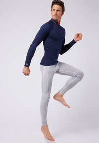 Marineblauw langemouwtop met textuurontwerp, gecombineerd met lichtgrijze leggings met ruitpatronen en contrasterende stiksels.