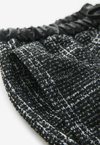 Tissu en tweed noir et blanc avec un tissage texturé, doté d'une taille froncée et de subtils accents métalliques.