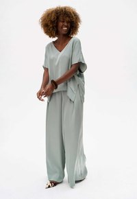 Licht teal twee-delig outfit bestaande uit een losse, kort-gevleugelde top en wijde broek met een gladde stofstructuur en zijsplitten.