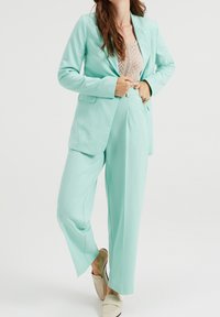 Sada mátově zeleného obleku, která obsahuje dobře střižený blejzr s klopovým límcem a kalhoty širokého střihu, vyrobené z hladké tkaniny s bočními kapsami.