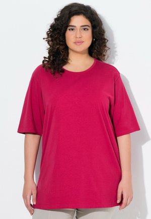 Magenta übergroßes T-Shirt, kurze Ärmel, runder Ausschnitt, Baumwollstoff, glatte Textur, minimale Nähte, getragen mit beigen Hosen.