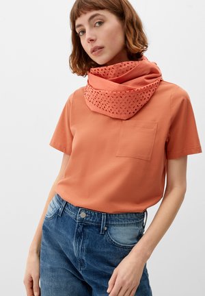 Koralle-orange T-Shirt mit kurzen Ärmeln und einer Brusttasche, getragen unter einem korallenfarbenen Schal mit Lochmuster, kombiniert mit hellblauen Jeans.