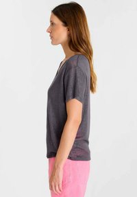 Donkergrijs T-shirt met korte mouwen en V-hals met een subtiele glans, gecombineerd met lichtroze broek, weergegeven in zijaanzicht.