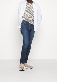 Lightweight white shirt over a gray and white striped t-shirt, paired with blue denim jeans and beige sneakers. Simple design, casual fit.