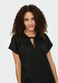 Črna bluzica s krožnim izrezom, nabranimi detajli in vezanjem. Kratki rokavi in mehak material; preprost in minimalističen dizajn.