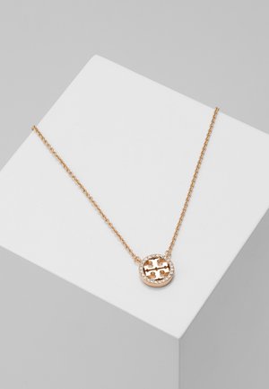 Gold chain necklace with a round pendant featuring a cross design and small crystals around the edge, displayed on a white surface.