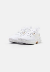 Pár bílých sportovních tenisek s síťovinou, šněrováním a jemnými béžovými akcenty na bílém pozadí.