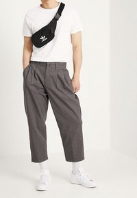 Black Adidas fanny pack, white t-shirt, gray high-waisted trousers, white sneakers, and white socks, all against a light background.