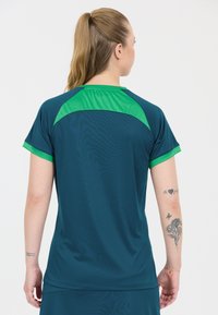 Teal atletisk skjorte med grønne accenter, korte ærmer og rund halsudskæring. Glat tekstur med et farveblokeringsdesign ved skuldrene.