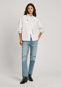 Vit skjorta med krage, bärs tillsammans med ljusblå slitna jeans och svarta ankelskor med klack.