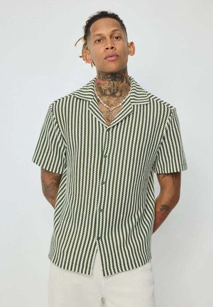 Chemise à manches courtes à boutons, à rayures vertes et blanches, avec un col campagnard et un tissu légèrement texturé. Comprend plusieurs boutons à l'avant.