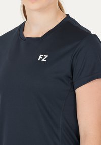 Marineblå sports T-shirt med v-hals, korte ærmer og hvid "FZ" logo på venstre bryst. Blødt, let stof med subtile sømme.