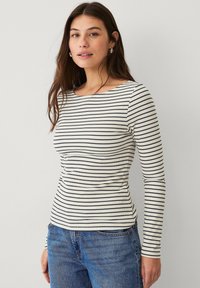 Langärmliges, leichtes Oberteil in Creme mit navyblauen horizontalen Streifen, Rundhalsausschnitt und geribbelter Textur, kombiniert mit Jeans.