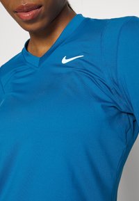 Zbliżenie na osobę w niebieskiej koszulce sportowej Nike z białym logo swoosh na piersi.