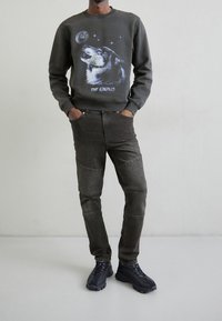 Gray sweatshirt featuring a wolf graphic and stars, paired with dark gray jeans with ribbed accents. Black textured sneakers complete the outfit.