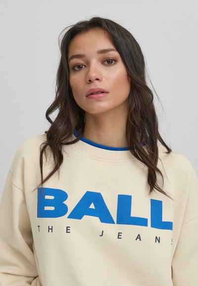 Sudadera beige con texto gráfico en azul y negro "BALL THE JEANS", cuello en azul acanalado y textura de tela suave.