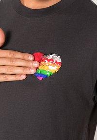 T-shirt nera a maniche corte con un design a cuore in paillettes multicolori sul petto, caratterizzato da tonalità vivaci e una superficie testurizzata.