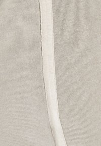 Gros plan sur un tissu tricoté beige avec une couture verticale centrale de couleur crème ou un détail côtelé.