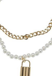 Chaîne en ton or superposée avec des perles blanches, dotée d'un pendentif en métal de forme courbée. Texture lisse avec une finition brillante.