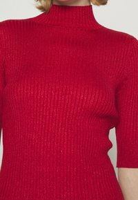 Röd ribbad stickad tröja med hög krage och korta ärmar, som har en blank yta och en figurnära design.