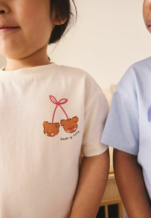 Zwei Kinder tragen Nahaufnahme-T-Shirts, eines cremefarben mit Bärengesichtern und dem Text "bear-y cute", das andere hellblau, beide stehen nebeneinander.