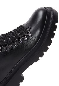 Botte en cuir noir avec semelle à crampons épaisse, œillets métalliques et lacets noirs conçue pour la durabilité et une utilisation en extérieur.