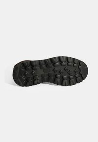 Zwarte rubberen buitenzool met diepe noppen en verschillende tractiepatronen, geschikt voor ruw terrein. Rond design van de neus.
