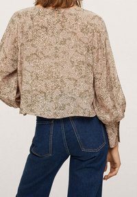 Luftig, cropped bluse i et lys beige stof med et grønt abstrakt mønster; har puffede ærmer og en lille nøglehul detail bagpå.