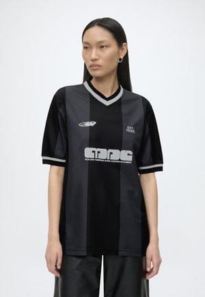 Femme asiatique aux longs cheveux noirs portant un maillot de sport rayé noir et gris foncé avec une bordure grise et un texte blanc imprimé.