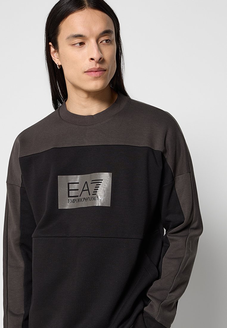 Felpa nera e grigia con patch del logo EA7 metallico, maniche lunghe, scollo rotondo e finitura in tessuto testurizzato.