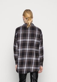 Camicia a scacchi bianca e nera con maniche lunghe, orlo arrotondato e accenti grigio chiaro. Tessuto leggero con un design a vestibilità ampia.