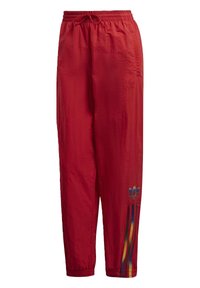 Červené sportovní kalhoty vyrobené z lehkého materiálu, s elastickým pasem, bočními kapsami a duhově pruhovanými detaily na nohavicích.
