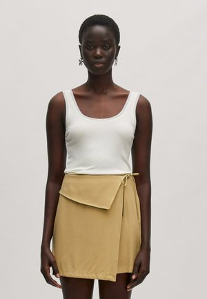 Witte geribde tanktop gecombineerd met een beige wikkelrok met een voorflap en strikdetail, gepresenteerd tegen een neutrale achtergrond.