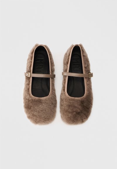 Ballerine marroni ricoperte di pelliccia con una texture morbida, punta tonda e una singola cinghia regolabile. Fodera interna nera e branding visibile.