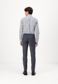 Chemise à boutons à motifs en bleu clair avec un design floral, associée à un pantalon gris foncé et des chaussures noires, vue de dos.