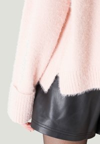 Hellrosa fuzzy Pullover mit geripptem Saum und Bündchen, mit einem V-förmigen Schlitz hinten, getragen über schwarzen Leder-Shorts.