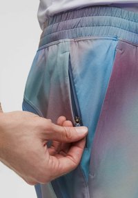 Pantalones cortos deportivos coloridos con un degradado de azul y morado, cintura elástica y un bolsillo lateral con cremallera. Textura de tela suave y lisa.