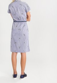 Randig kortärmad klänning med blommig broderi, åtsittande midja, knälång skärning och mjukt, lätt tyg. Bär mörkblå sneakers.