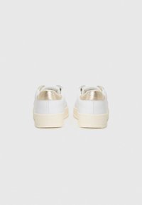 Sneakers bianchi con tomaia in pelle liscia, accenti metallici dorati sul tallone e suola in gomma color crema. Design minimalista.
