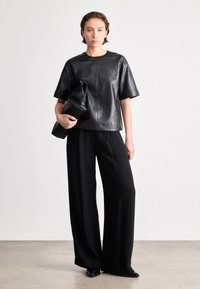 Top de pele preta de manga curta combinado com calças largas pretas. O top apresenta um decote redondo e uma textura suave.