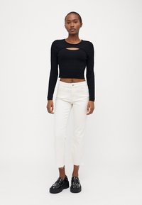 Black ribbed crop top with a cutout detail, paired with white straight-leg jeans and black platform shoes adorned with studs.