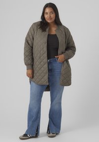 Quilted olive green jacket with a rounded collar, snap buttons, and ribbed cuffs, paired with light blue flared jeans and sneakers.