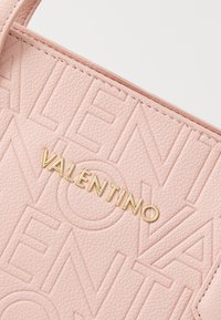 Rozā teksturēta ādas rokassoma ar izvirzītiem burtiem un zelta logo, gluda apdare un kontrastējošas šuves detaļas.